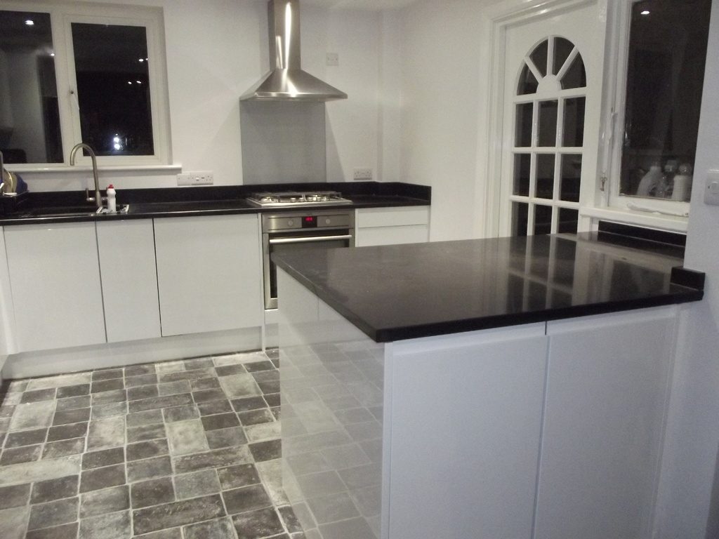 A bright white kitchen with a black stone island and an arched glazed door